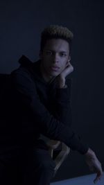 Portrait of young man sitting against black background