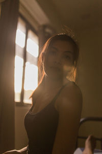 Portrait of young woman while standing by window at home