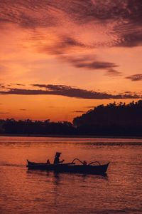 Silhouette people in boat against sky during sunset