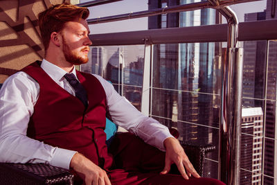 Young man looking away while sitting on window