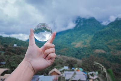 Cropped hand holding crystal ball against mountain