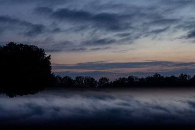 Silhouette trees against dramatic sky during sunset