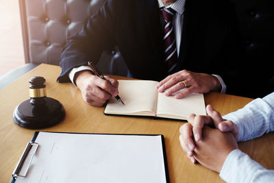 Cropped image of judge writing in book while nervous client sitting at desk