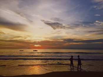 Silhouette people standing on beach against sky during sunset