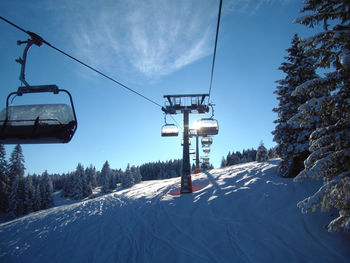 Ski lift over snow covered field against sky