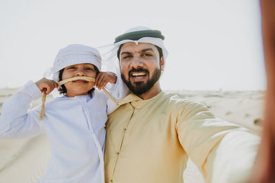 Portrait of father and son doing selfie while standing at desert