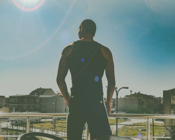 Rear view of man standing by railing against sky