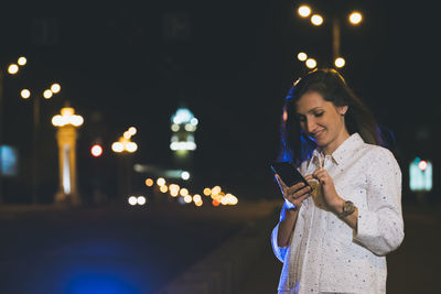 Portrait of young woman holding illuminated string lights at night