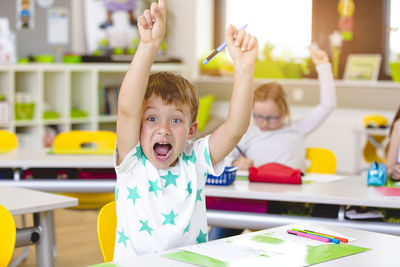 Portrait of boy with arms raised in classroom