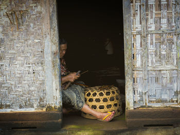 Senior woman cutting stick while sitting by basket in house