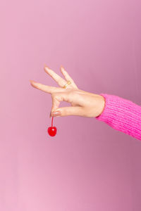 Female hand wearing pink sweater and holding a cherry. light pink background.