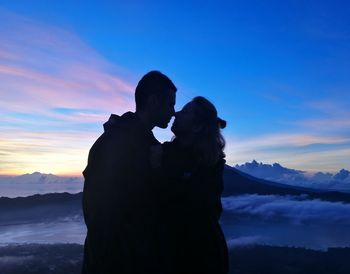 Silhouette couple standing on mountain against sky during sunset