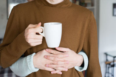 Cropped hands of man embracing boyfriend holding cup