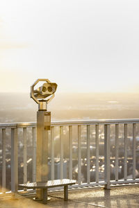 Coin-operated binoculars by railing against clear sky