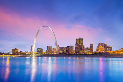 Illuminated city by river against sky