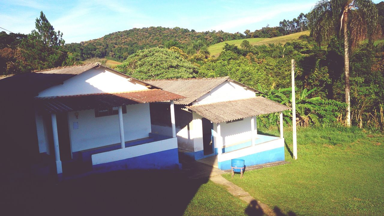 grass, building exterior, tree, built structure, house, architecture, sky, landscape, mountain, sunlight, tranquility, tranquil scene, field, nature, green color, day, shadow, scenics, beauty in nature, growth