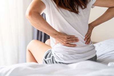 Midsection of woman sitting on bed at home