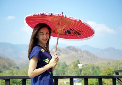 Young woman holding red while standing on mountain against sky