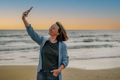 A young woman on the beach near the ocean in the spring at sunset takes a selfie, talks via video