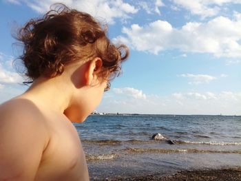 Side view of shirtless boy standing at beach against sky