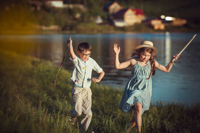 Girl and boy holding stick running by lake