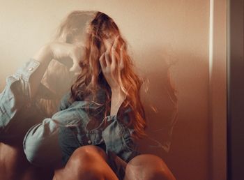 Double exposure of woman sitting by wall