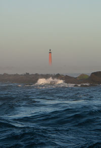 Lighthouse by sea against clear sky