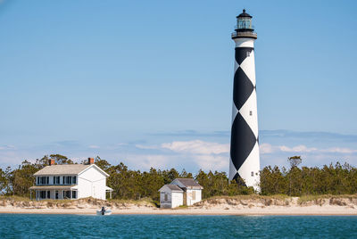 Lighthouse by sea against buildings against clear blue sky