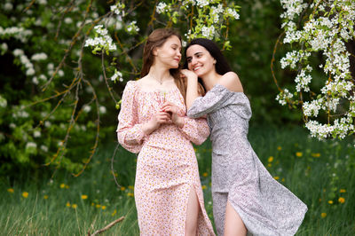 Two young girls in dresses are standing under a white tree laughing and looking away
