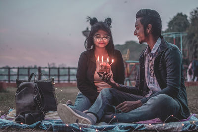 Young couple sitting on retaining wall against sky