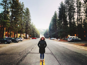Full length of woman wearing fur hat standing amidst road against trees