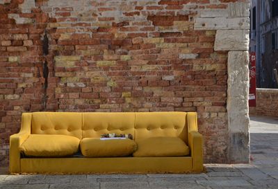 Empty sofa against brick wall on sidewalk