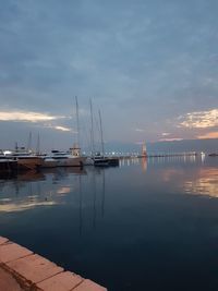 Sailboats moored at harbor against sky during sunset