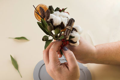 Woman holds small bouquet with cotton flowers and dry orange slices above table