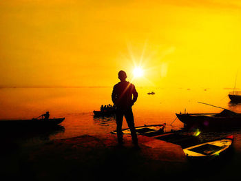 Silhouette man standing on beach against orange sky