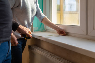 Young couple moving in new apartmen. people measure size of window sill with a tape measure. 