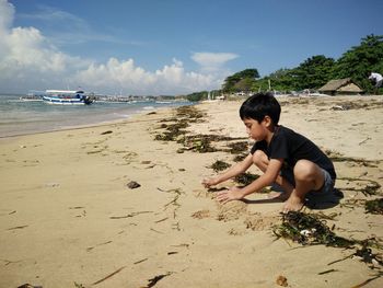Full length of playful boy at sandy beach against sky