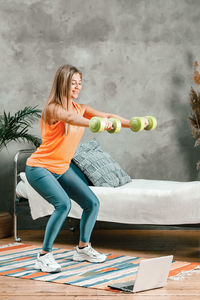 Cheerful sporty woman with blond hair doing a squat with dumbbells and watches 