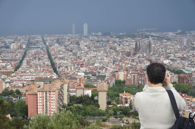 Rear view of man photographing sagrada familia amidst cityscape