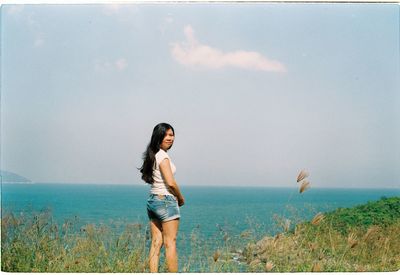 Young woman standing by sea against sky