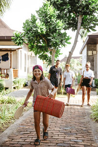 Happy girl holding mat while walking on footpath with family at tourist resort