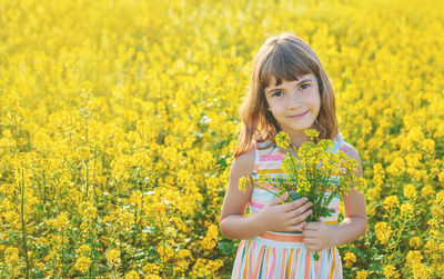 Portrait of cute girl holding flowers while standing in field