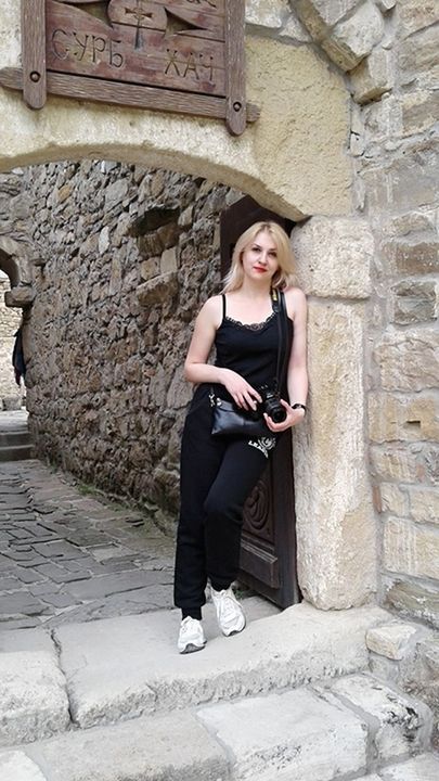 one person, full length, architecture, young adult, front view, leisure activity, young women, real people, wall - building feature, lifestyles, built structure, casual clothing, day, wall, building exterior, holding, smiling, clothing, stone wall, hair, hairstyle, fashion, outdoors, beautiful woman