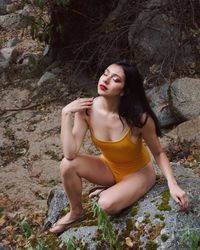 Sensuous young woman sitting on rock in forest