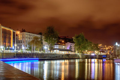 Illuminated buildings by river against sky at night