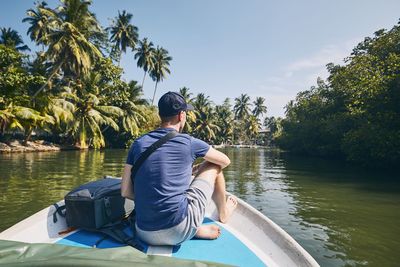 Rear view of man sitting on rowboat in lake at forest