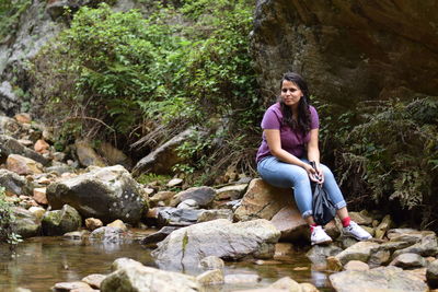Portrait of young woman sitting on rock by stream