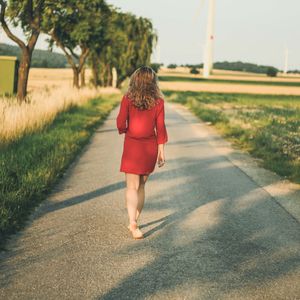 Rear view of young woman walking on footpath amidst grassy field