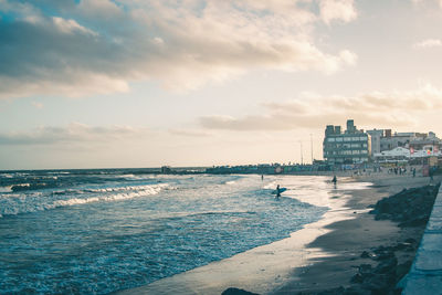 Scenic view of surfers in sea against cloudy sky