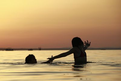 Girls swimming in sea against sky during sunset